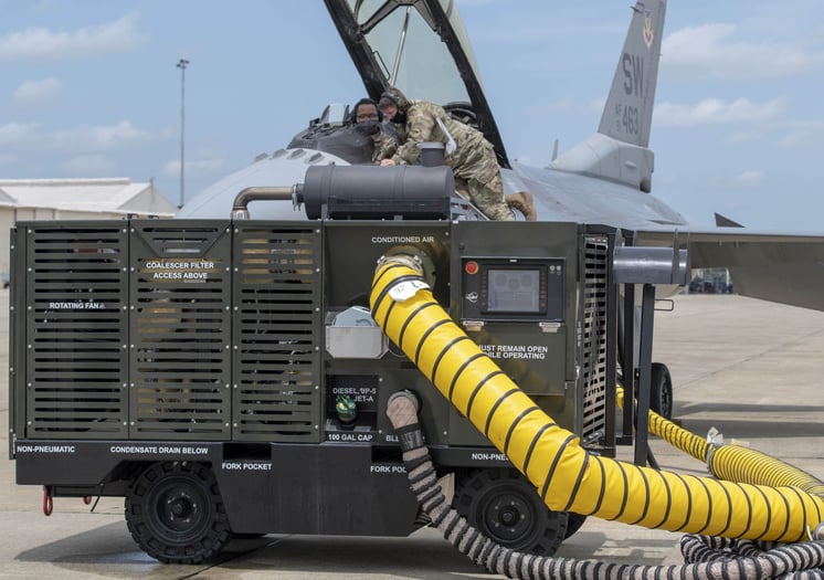 An AgileAir® ground support cart in use outdoors, connected to a fighter jet via a yellow hose