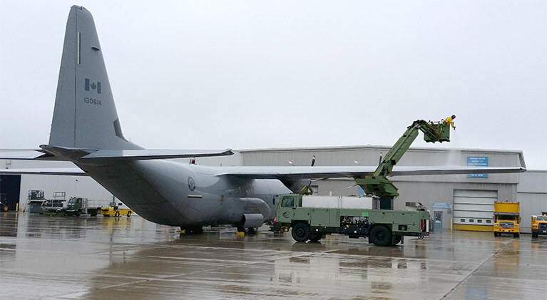 A green Tempest Deicer de-icing a grey airplane at an airport