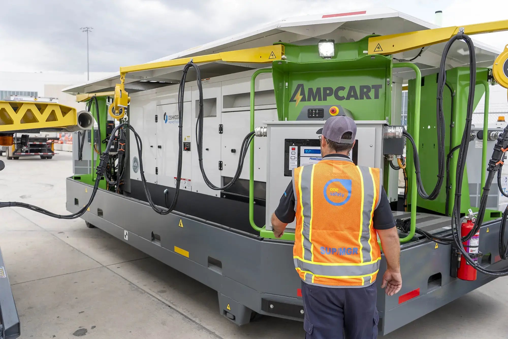 Operator wearing an orange vest next to AmpCart at airport