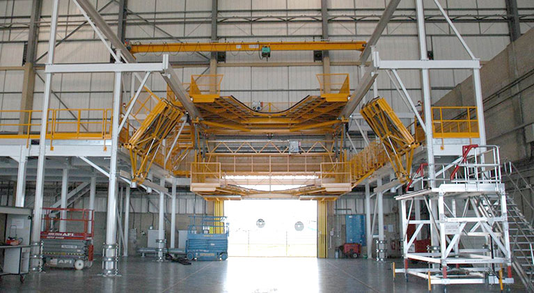 A spacious hangar with a suspended yellow scaffolding system, featuring adjustable platforms designed for aircraft maintenance.